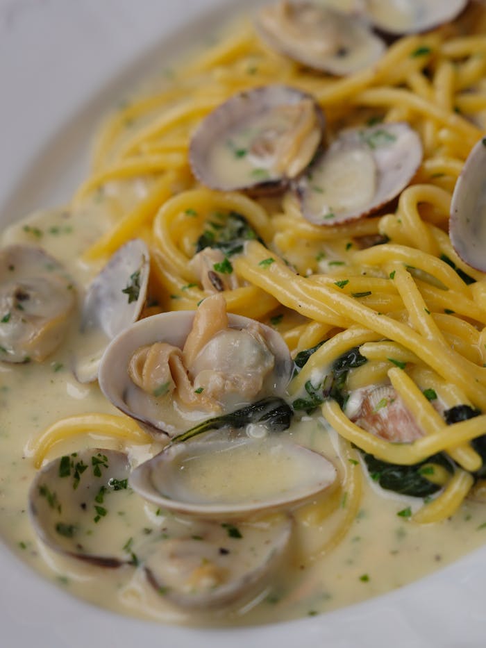 Capture of linguine pasta in creamy sauce topped with fresh clams. Perfect for seafood lovers.