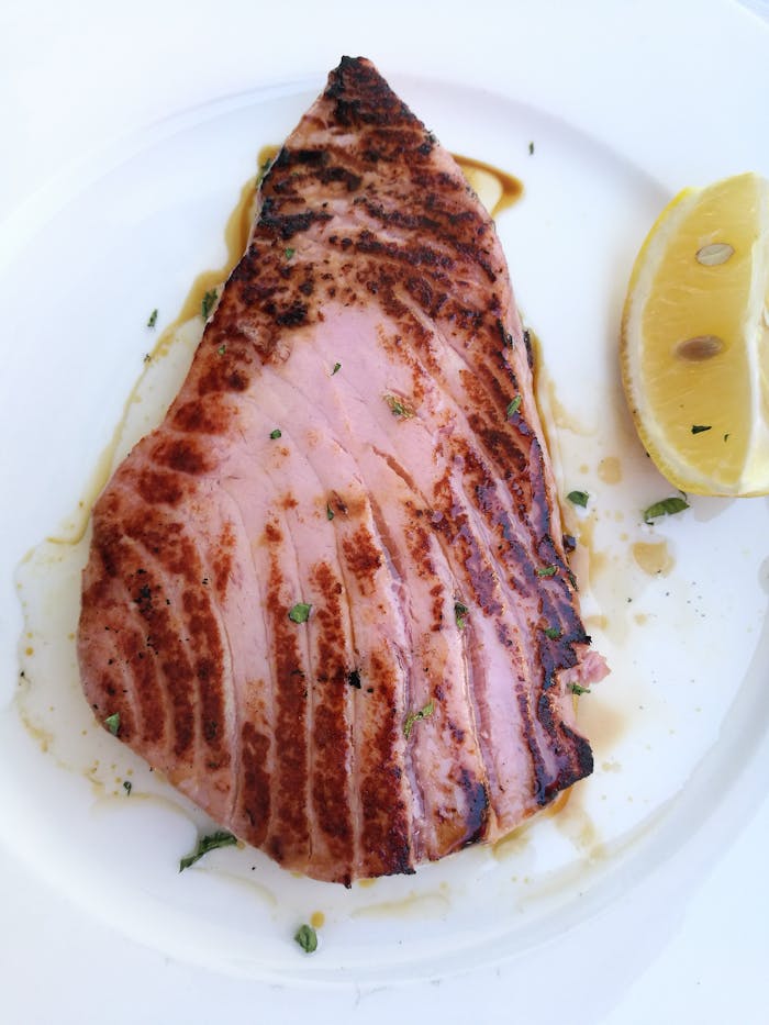 about-us-02 Close-up of a grilled tuna steak served with a lemon wedge, perfect for seafood enthusiasts.